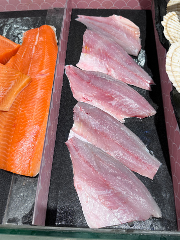 Stock photo showing close-up, elevated view of a retail seafood display with Atlantic salmon fillets and red snapper steaks on chilled metal tray.