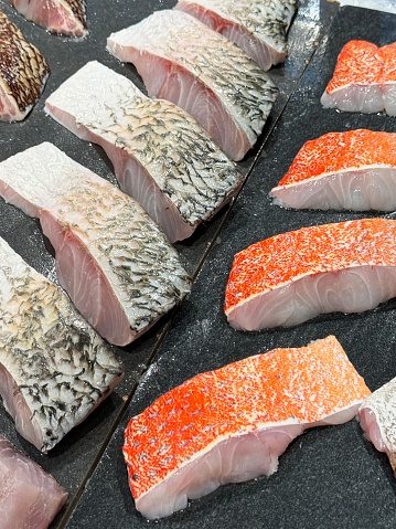 Stock photo showing close-up, elevated view of a retail seafood display with sea bass, red grouper and red snapper steaks on chilled metal tray.