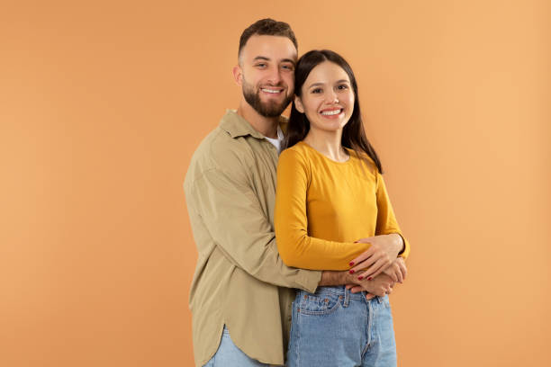 istock Happy young man hugging his girlfriend posing on orange background 2060390213