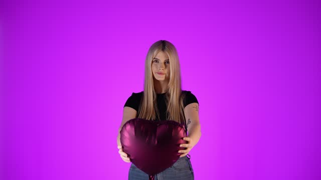 Cute blonde woman shows red balloon heart, concept of giving love as a gift