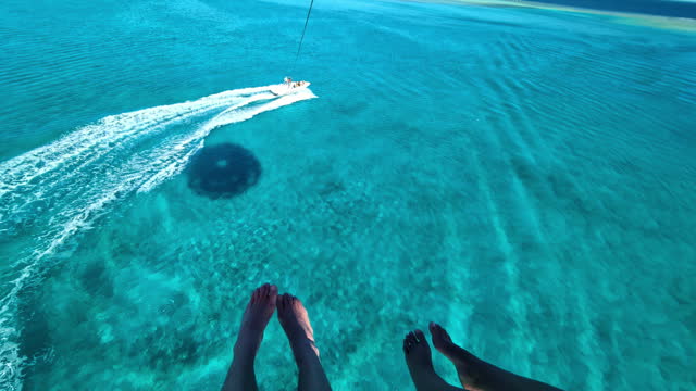 POV View of Couple Parasailing with the Speedboat in the Turquoise Blue Waters Below.
