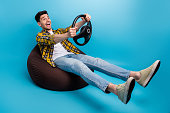 Full length photo of young guy without driver license in pouf holding steering wheel look like f1 racer isolated on blue color background