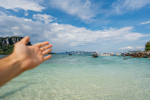 Young man's hand as he is showing the beautiful beach on the Andaman sea in Thailand. His POV.