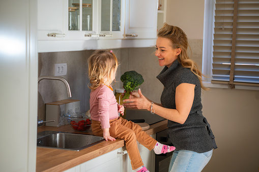 Happy mother and her little daughter are preparing broccoli for lunch in the kitchen