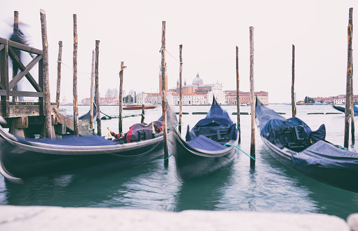Gondolas tied up on the side of a misty Grand Canal in Venice. Across the water we see the iconic shape of the Church of San Giorgio Maggiore