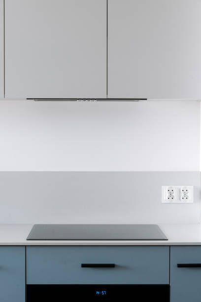 Modern household appliances at domestic kitchen. Glass ceramic induction stove, oven with timer, integrated range hood and cabinet furniture in minimalist style.