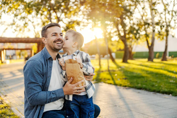 A boy is kissing his father in a park.