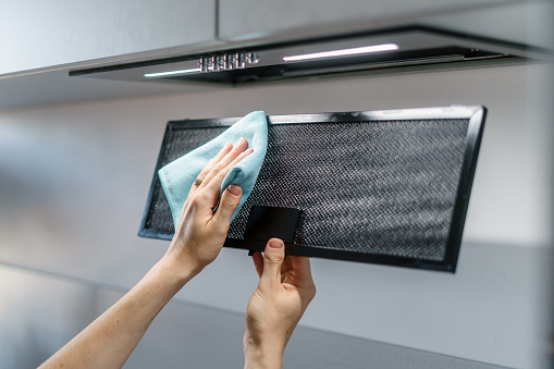 Cropped shot of woman cleaning aluminum mesh filter, wipe dirty part of black metal kitchen hood extractor with cloth, side view. Concepts of maintenance household alliance and housework