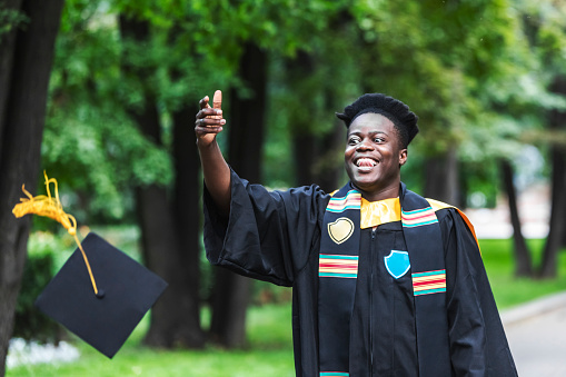 Young adult black man in university graduate black gown throwing up cap