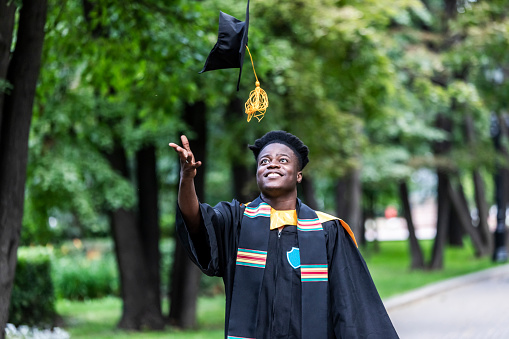 Young adult black man in university graduate black gown throwing up cap