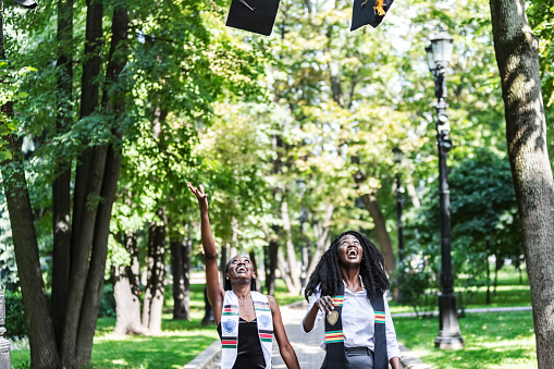 Two Black Female University Graduates wearing black gown trowing up caps