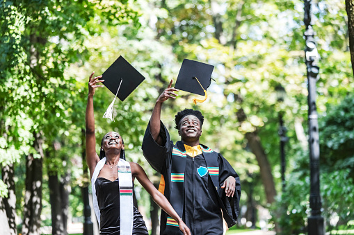 Black Female and male University Graduates in black gown throwing up cap