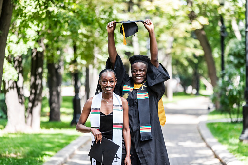 Black Female and male University Graduates in black gown throwing up cap