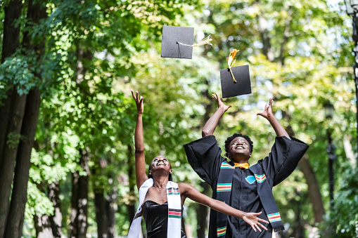 Black Female and male University Graduates in black gown throwing up cap