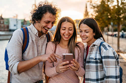 Three young friends using smart phone in Copenhagen in Denmark.