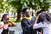 Young man helping young woman to put on graduate gown and cap