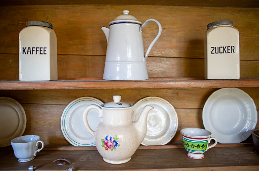 Old-fashioned plates, cups, coffee pots and coffee and sugar containers on a wooden shelf