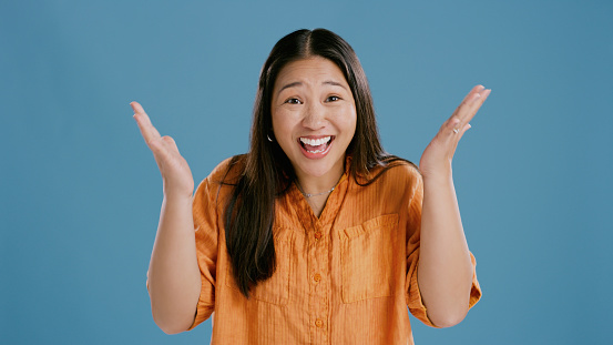 Asian woman, studio and surprised with happiness in blue background, announcement and competition winner. Female person, smile and excited to choose with opportunity, options and giveaway offer.