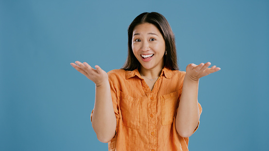 Asian woman, studio and comparison with smile for decision in blue background, ideas and confused with choice. Female person, mock up and happy to choose with options, pick and showing offer.