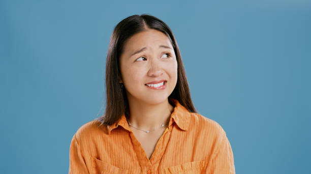 Woman, thinking and studio for choice of education by blue background or decision or confused. Japanese student, excited or nervous for planning with scholarship and mock up for option of university Woman, thinking and studio for choice of education by blue background or decision for career. Japanese student, excited and nervous for planning with scholarship in mock up and options for university biting lip stock pictures, royalty-free photos & images
