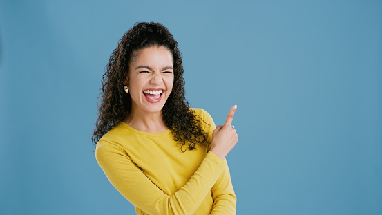 Pointing up, funny or happy woman with sale, promotion offer or discount deal isolated in studio. Excited, smile or person laughing with advice mockup space, news or menu choice on blue background