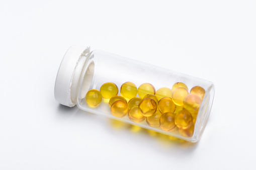 A transparent vial with yellow capsules lies on a light background close up isolated
