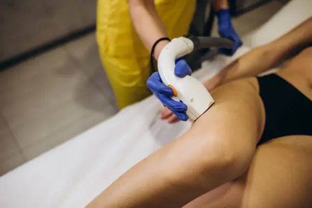 Close-up of a female cosmetologist in a medical coat making a young woman a procedure laser hair removal for leg. Cosmetology, ionization, diamond procedures