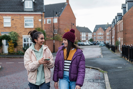 Two sisters spending time together outdoors, laughing and talking on a walk, using a mobile phone together. They are in the North East of England.