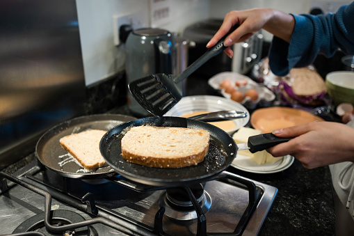 Close up of a teenage girl cooking  in her kitchen at her home in the North East of England. She is making French toast, frying it in a frying pan.