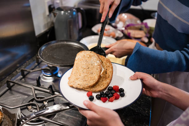Two sisters cooking together in a kitchen at their home in the North East of England. They are making French toast, plating it from a frying pan.