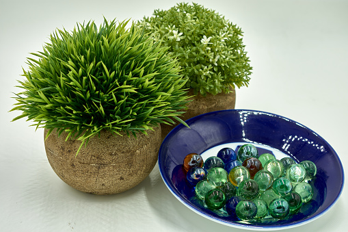 Two small rounded green artificial plants next to a group of glass marbles