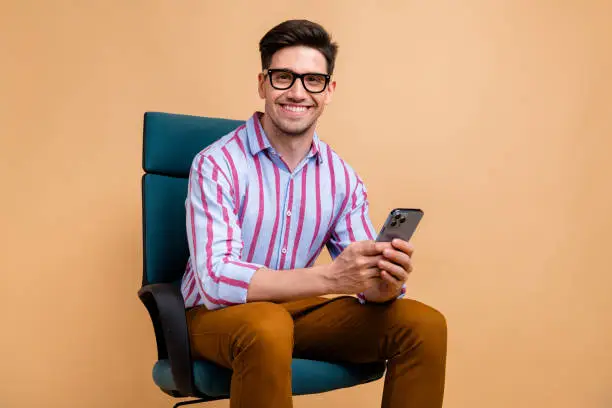 Photo of Photo of responsible man lawyer banker wear trendy clothes sit chair hold gadget device iphone samsung isolated on beige color background