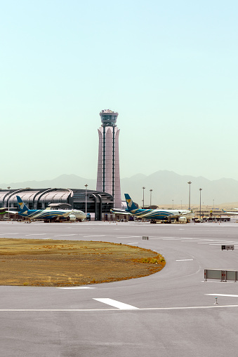 Muscat, Oman - May 22, 2023: Muscat airport control tower. Oman Air planes at the boarding gates of the airport in Muscat. Sultanate of Oman