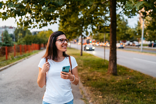 Beautiful young woman using smart phone while walking near a elementary school on a sunny day.