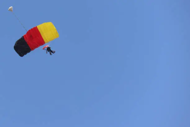 Tandem skydiving (parachuting) on a clear blue sky day, with the parachute decorated in the Germany flag colors