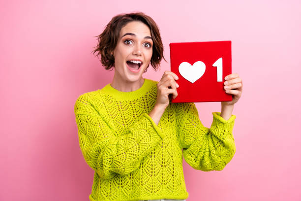 istock Photo of young blogging amazed woman in knitted pullover holding red cube button plus one like content isolated on pink color background 2060576725
