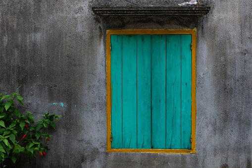 Turquoise blue wooden shutter slats with a yellow frame on a window of a rural home in northern Vietnam.