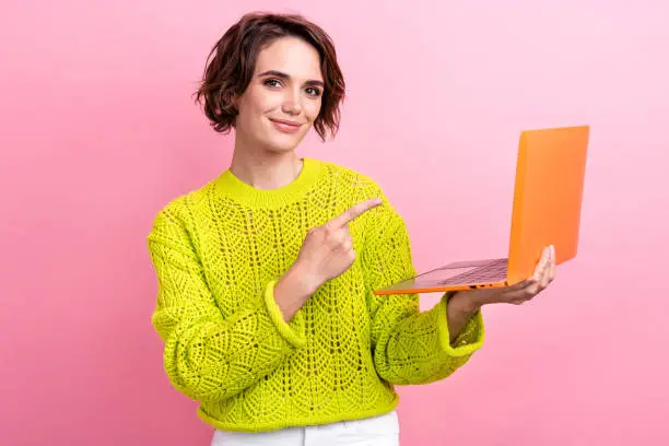 Photo of young woman wear knitted sweater direct finger showing modern technology rtx nvidia in laptop isolated on pink color background.