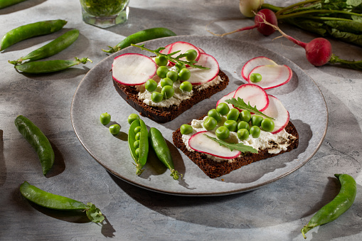 Open sandwich with cream cheese, green pea , radish and arugula on gray background. Vegetarian sandwich on rye bread with vegetables.