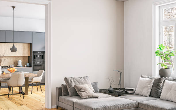 A modern home interior: a living room with a grey sofa in front of a white blank wall and a window with a cityscape view in the foreground, a modern light grey kitchen and a full dining table with chairs in the background
