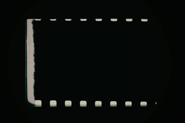 Black background with original 35mm film reel with empty dusty frames or cells and nice texture on the border, fluff on the film stock, real film grain