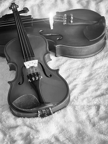 Small violin put in front of blurred bigger one,on soft cotton cloth,show detail of acoustic instrument.black and white tone,Lens flare effect