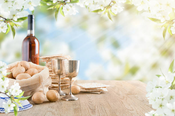 passover celebration concept. matzah, red kosher and walnut on wooden vintage table table in front of spring blossom tree garden and flowers landscape with sun rays with copy space. mock up. - passover matzo wine wine bottle стоковые фото и изображения