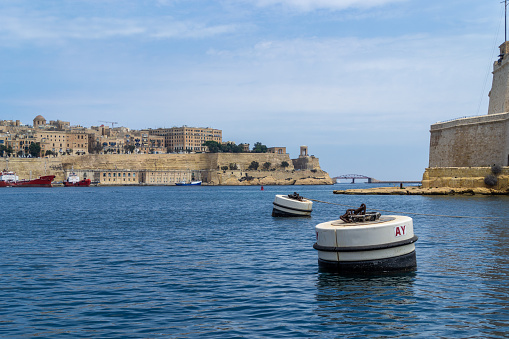 Valletta, Malta - June 10th 2016: Buoys in the Grand Harbour next to the tip of Fort St. Angelo. In the background is the city of Valletta with Pixkerija, Lower Barrakka Gardens and Siege Bell Memorial.