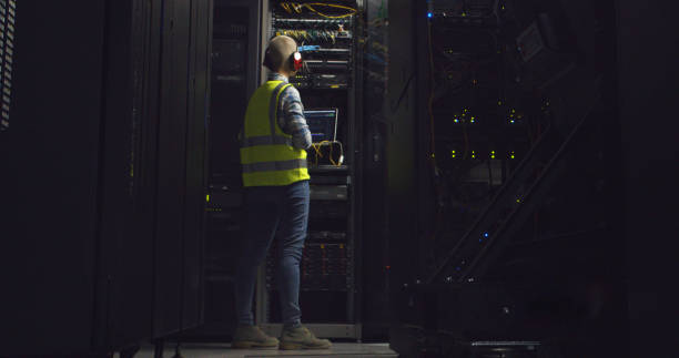 istock Technician, computer and server room for cables inspection, hardware and maintenance in engineering. Back of person with laptop in night data center for coding, backup and cybersecurity with mock up 2060663797
