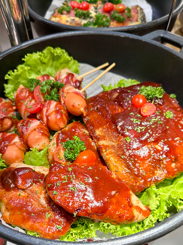 Stock photo showing close-up, elevated view of a meal of Chinese pork salad, with barbecue sauce, being served in a handled, metal cooking pot lined with greaseproof paper.