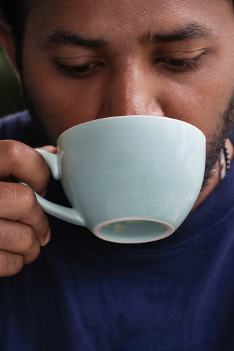 Stock photo showing close-up view of a cup of cappuccino coffee being drunk from a pale blue saucer. The freshly brewed coffee is being served in a cafe.