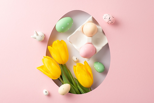 Greet spring with an Easter-themed layout. Top view of bright tulips, rabbit silhouette, rainbow-hued eggs in pottery dish, peeking through ovular opening on gentle pink surface, space for custom text