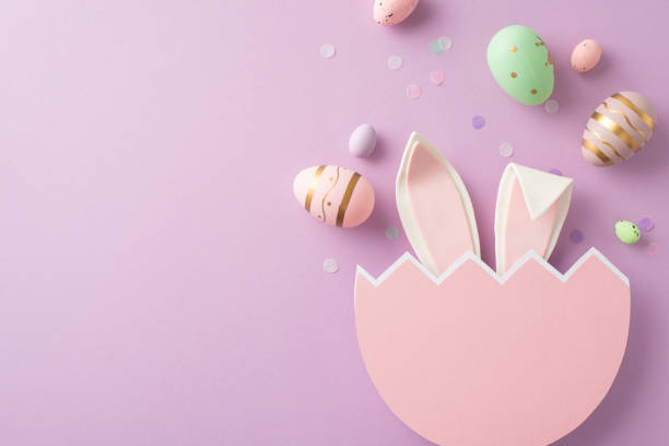 istock Easter joy creatively captured from top view, including eggs in every shade, bunny ears from a broken egg, and confetti on a lilac background, with space for wording 2060685074