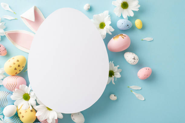 istock Springtime charm captured in top view photo: pastel-colored eggs, bunny ears, fresh daisies on a soft blue backdrop, complemented by a cut-out card in the shape of an egg for heartfelt Easter messages 2060685591